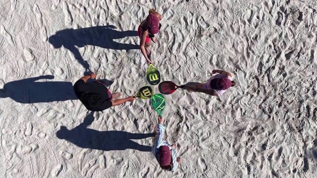 Grupo reunido com raquetes na quadra de areia, visto de cima